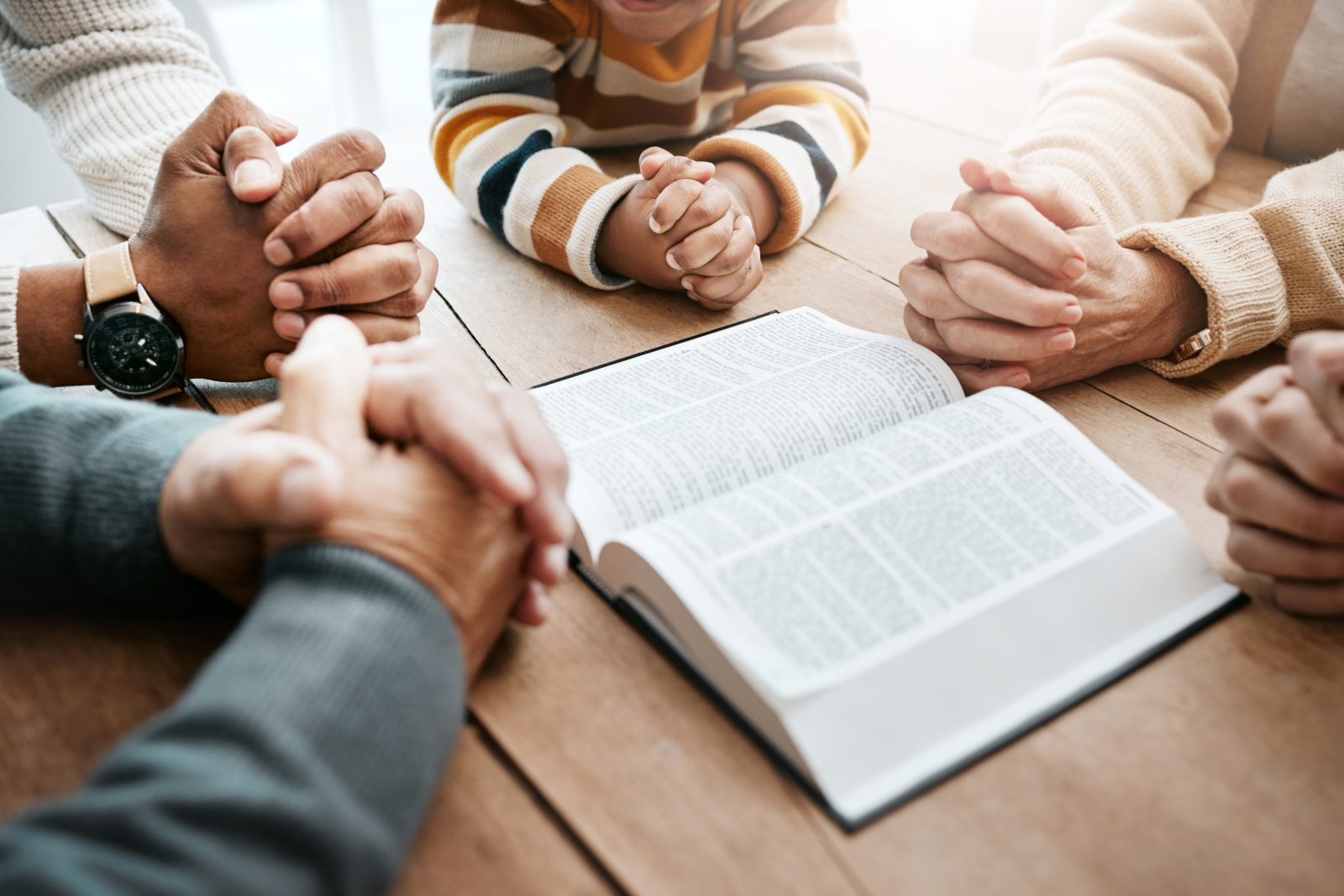 Bible, reading book or hands of big family in prayer, support or hope in Christian home for worship together. Mother, father or grandparents studying, praying or asking God in religion with children.