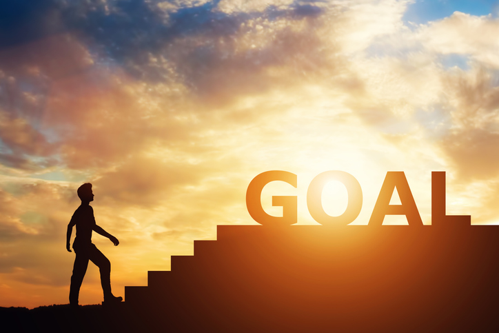 Man standing in front of stairs with "goal" writing on top. Money pursuit. Aspirations.