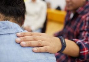 Closeup of young man crying in support group with psychologist comforting him, copy space